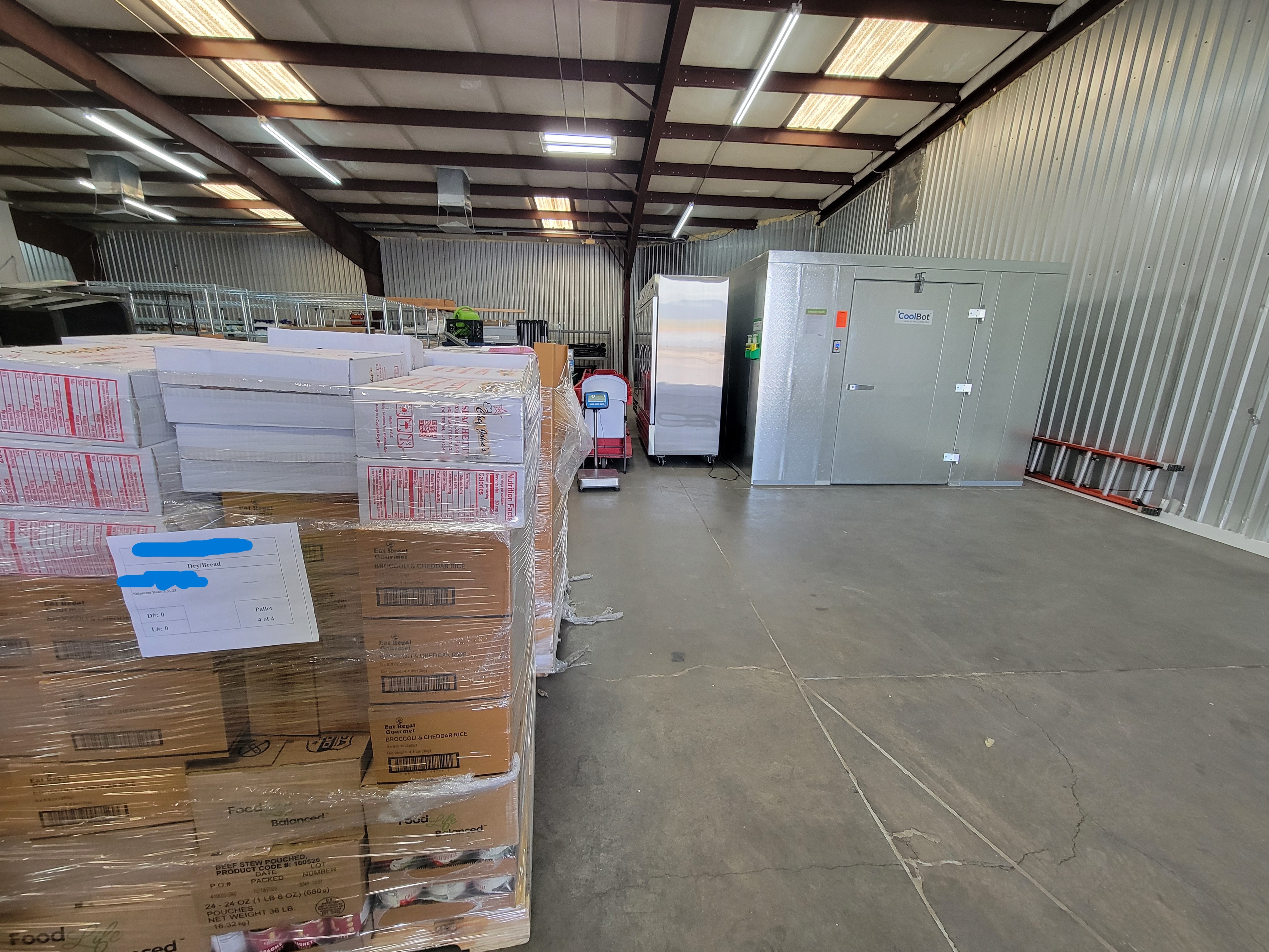Warehouse with pallets of food to the left and a fridge box unit to the right.